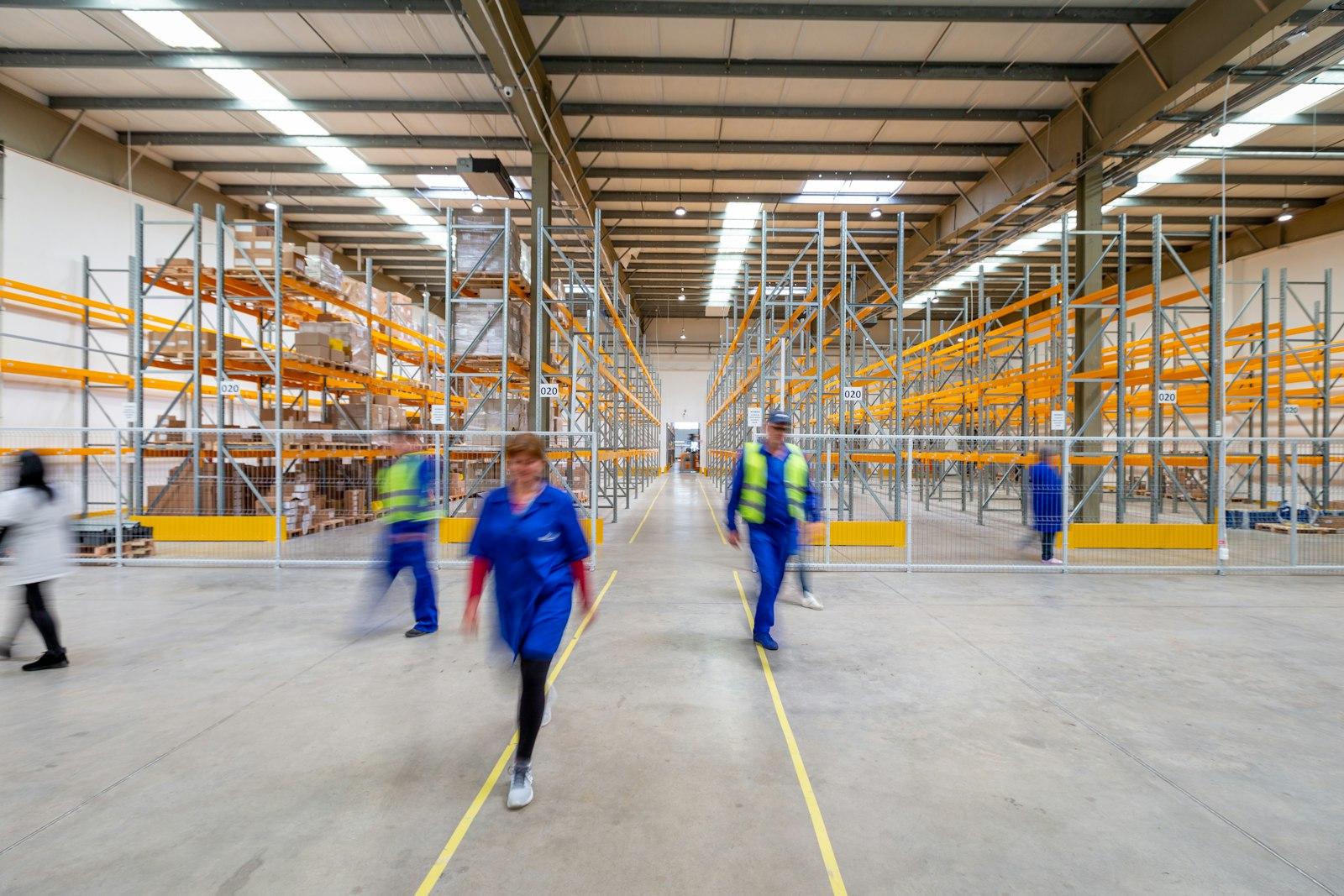 Workers walking through a large distribution warehouse with racking on either side